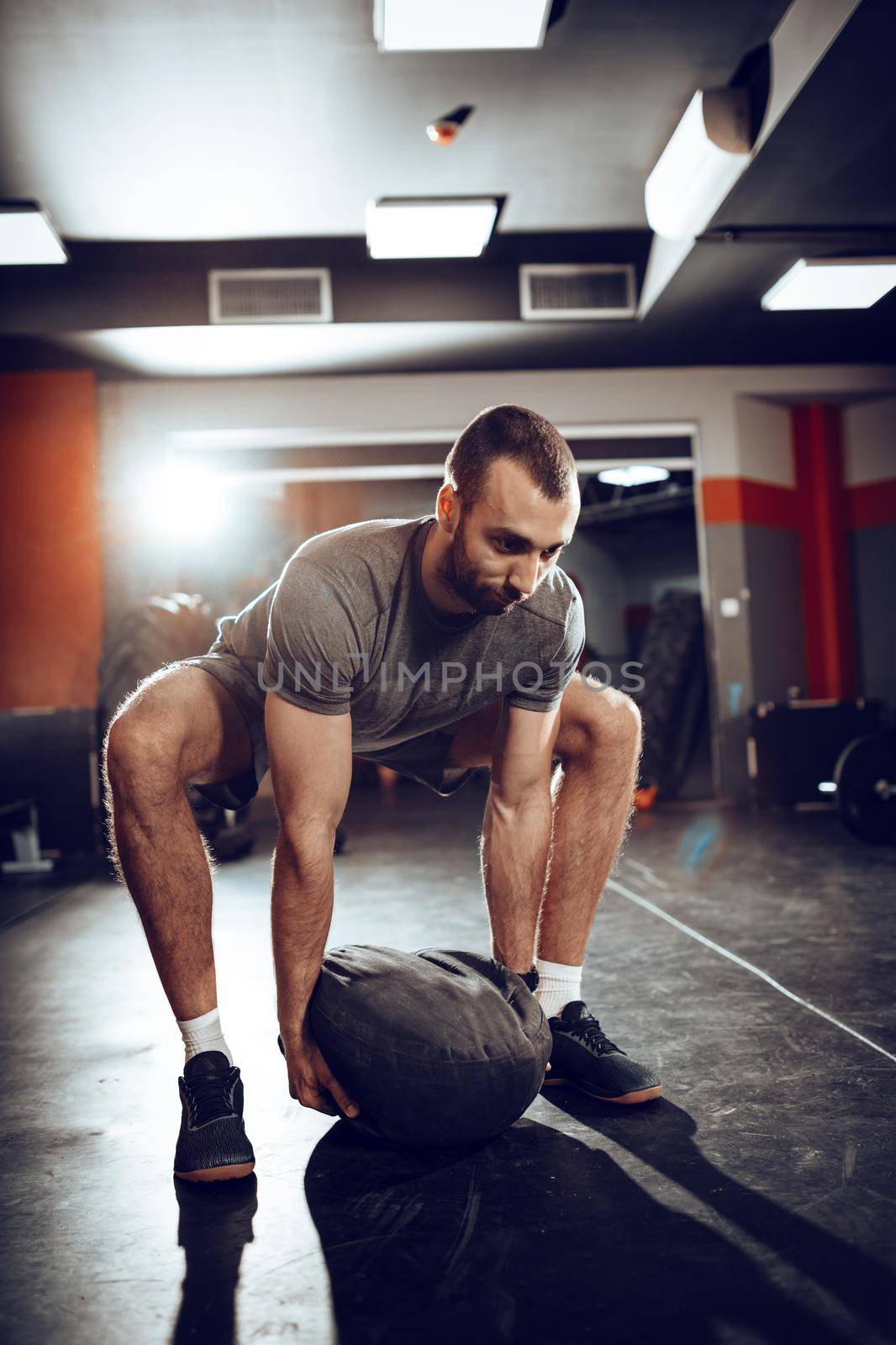 Strong man doing cross training with sandbag at the gym.