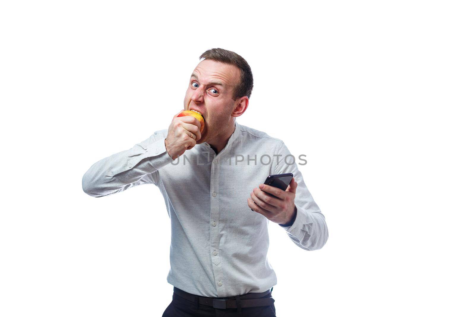 Caucasian male businessman holding a mobile phone in black and holding a red-yellow apple. He is wearing a shirt. Emotional portrait. Isolated on white background