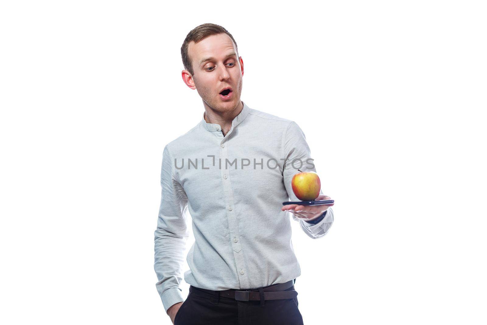 Caucasian male businessman holding a mobile phone in black and holding a red-yellow apple. He is wearing a shirt. Emotional portrait. Isolated on white background by Dmitrytph