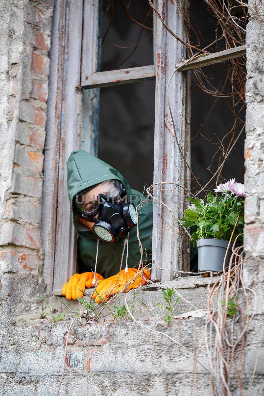 A man in a raincoat and gas mask collects a flower from a scorched, poisonous earth. Air pollution concept. Ecological catastrophy.