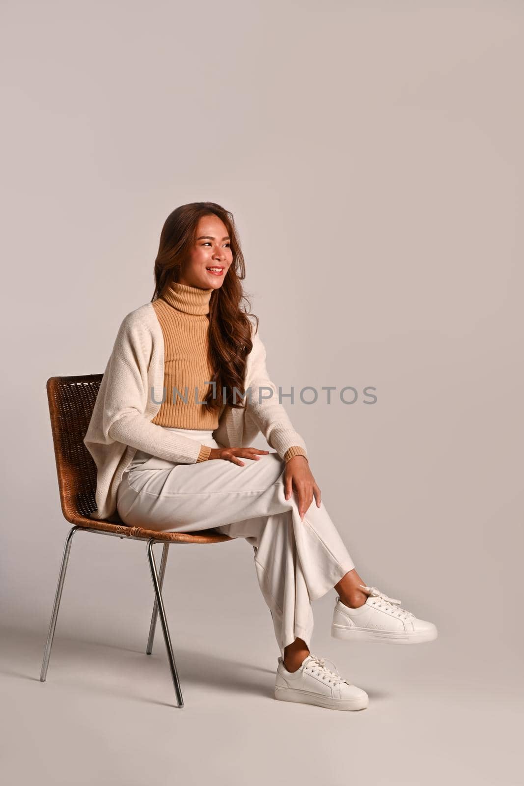 Full length portrait of beautiful woman wearing warm sweater sitting on a chair over white background. Studio shot.