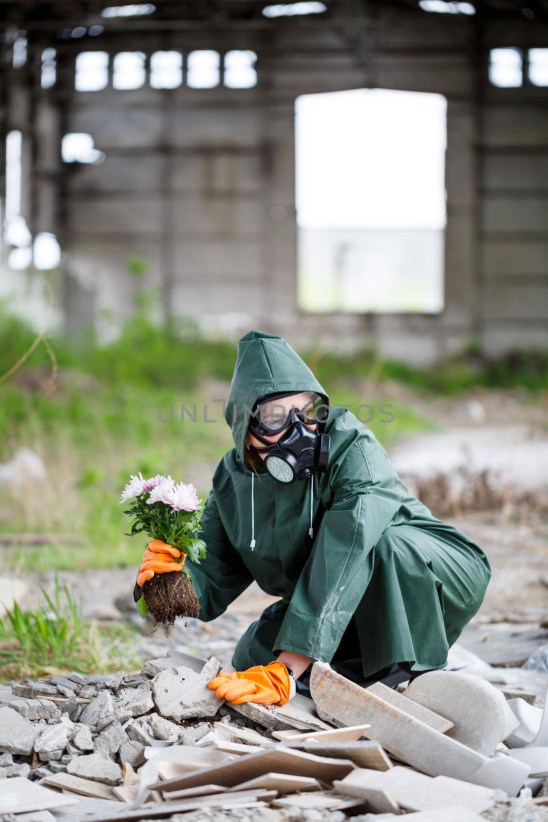 A man in a raincoat and gas mask collects a flower from a scorched, toxic land. Air pollution concept. Ecological catastrophy.