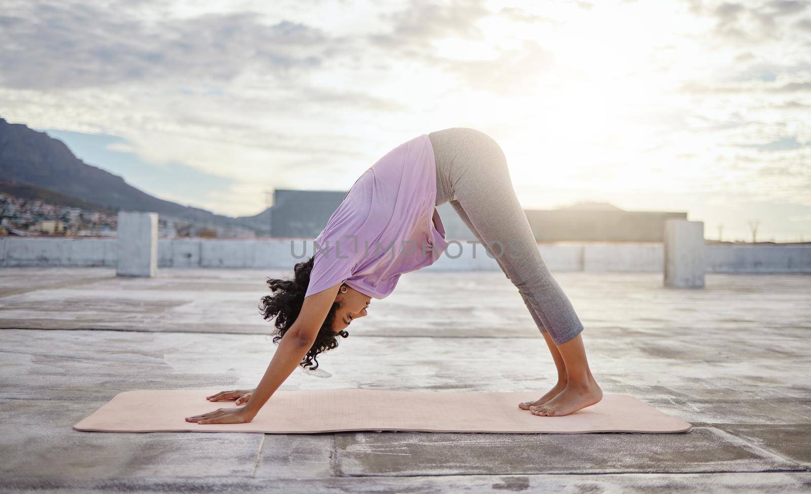 Yoga exercise, city rooftop and woman bending down for balance, wellness and health on an urban building in the morning. Fitness girl training and active during a healthy workout against overcast sky.