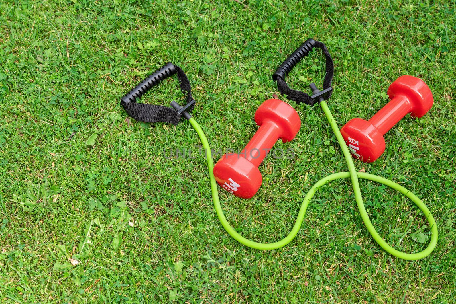 Ladie's dumbbells and fit tube the green grass background, top view. Outdoor training concept. Copy-space.