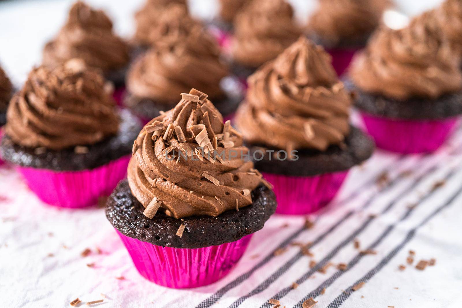 Piping chocolate ganache frosting on top of chocolate cupcakes.