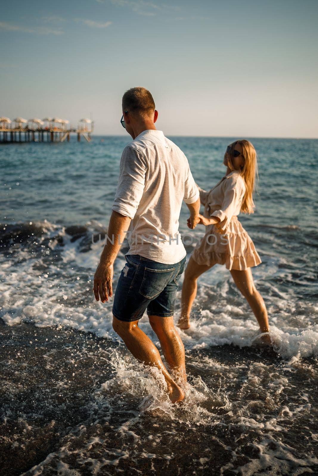 romantic young couple in love together on the sand walks along the beach of the Mediterranean sea. Summer vacation in a warm country.