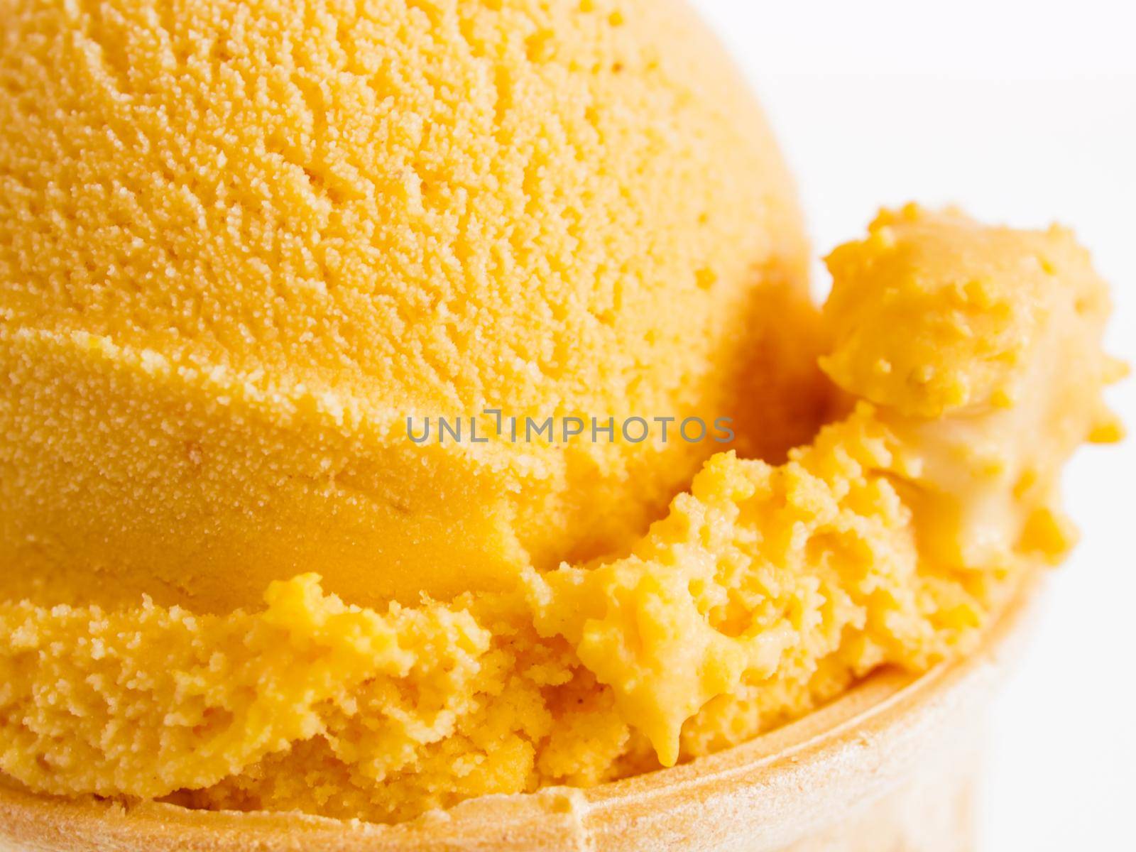 Scoop of gourmet pumpkin gelato in cake cone on white background.