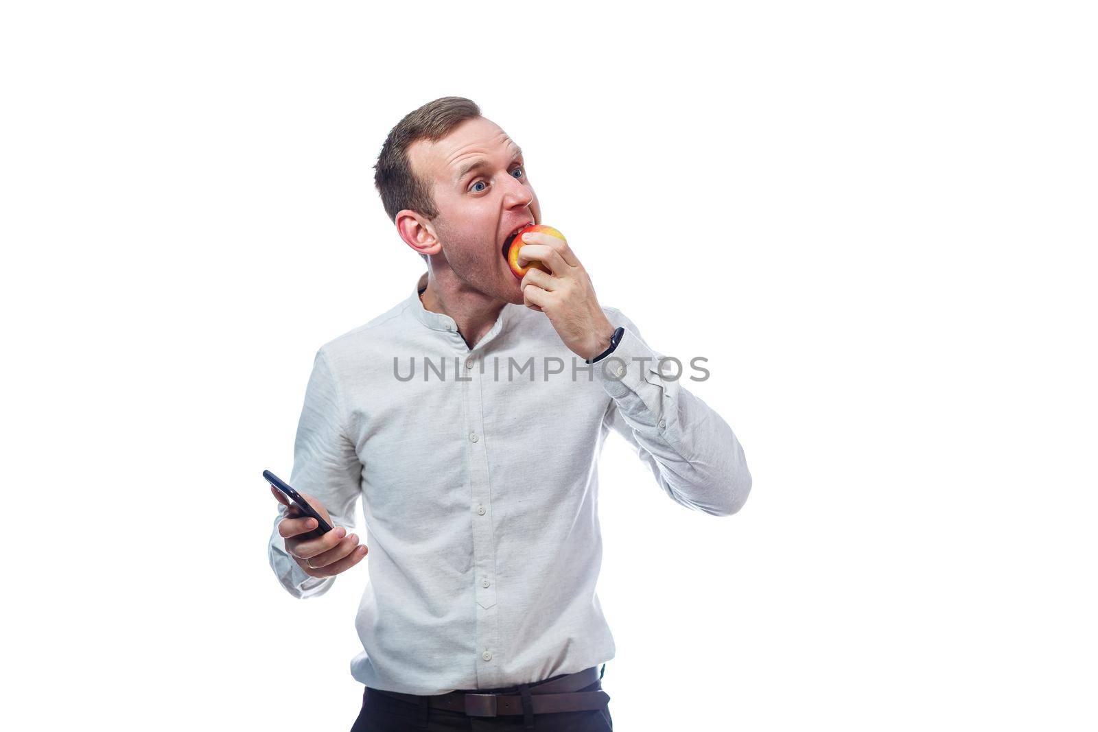 Caucasian male businessman holding a mobile phone in black and holding a red-yellow apple. He is wearing a shirt. Emotional portrait. Isolated on white background by Dmitrytph