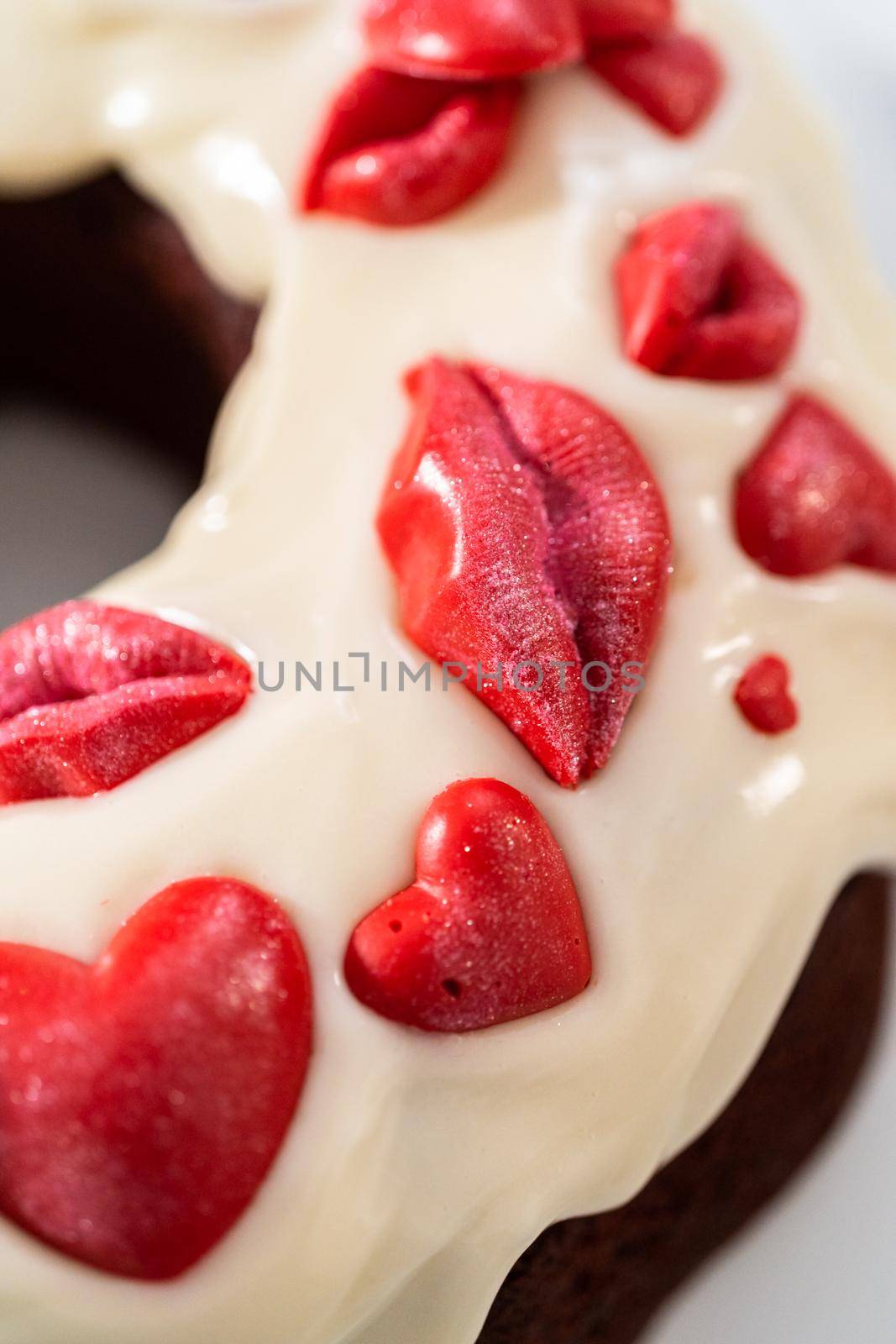 Freshly baked red velvet bundt cake with chocolate lips and hearts over cream cheese glaze for Valentine's Day.