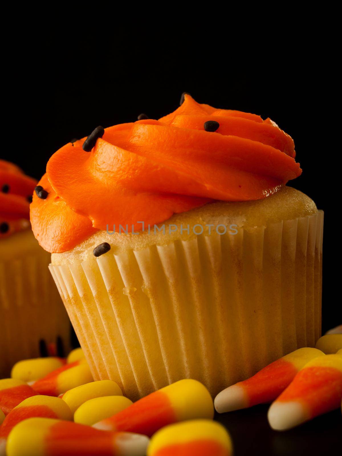 Halloween orange and black cupcakes with candy corn candies on black background.