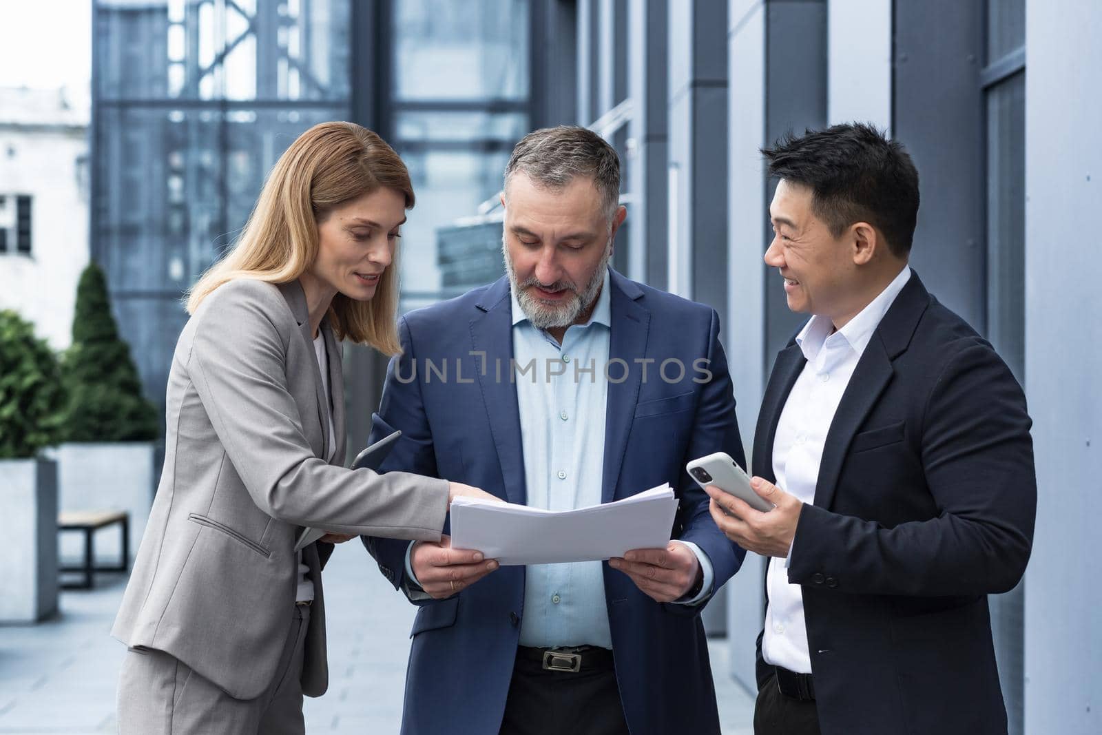 Three businessmen outside office building with documents discussing plans by voronaman