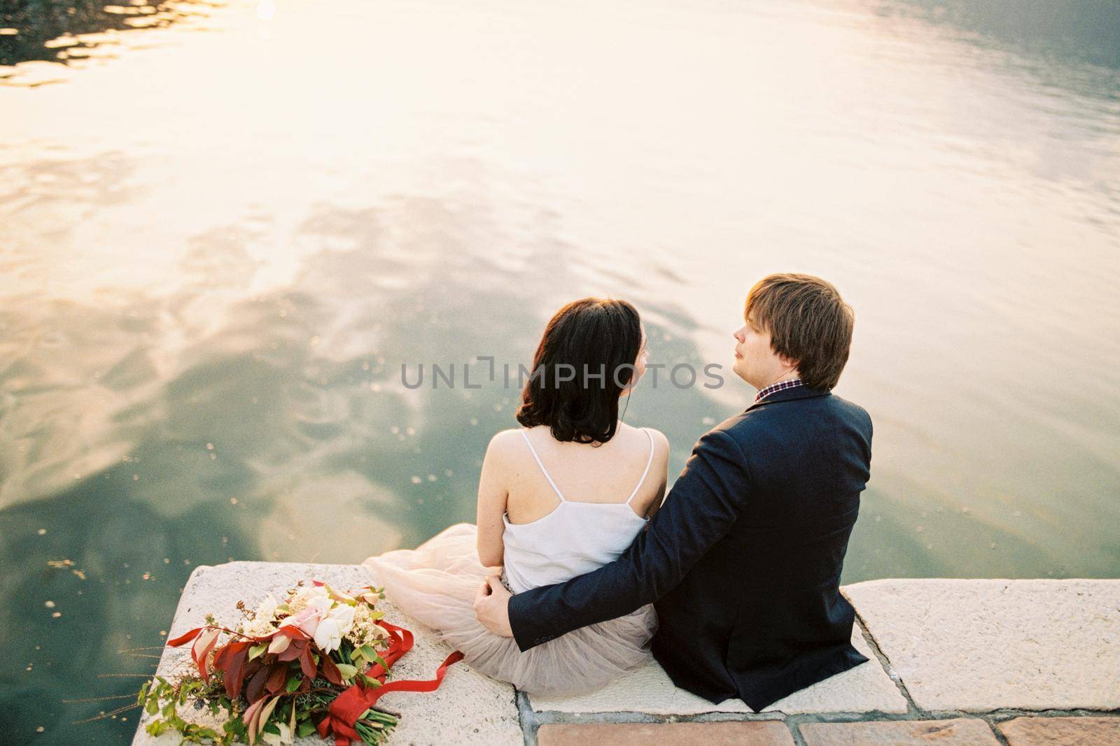 Bride and groom hugging sitting on the pier by the sea. High quality photo
