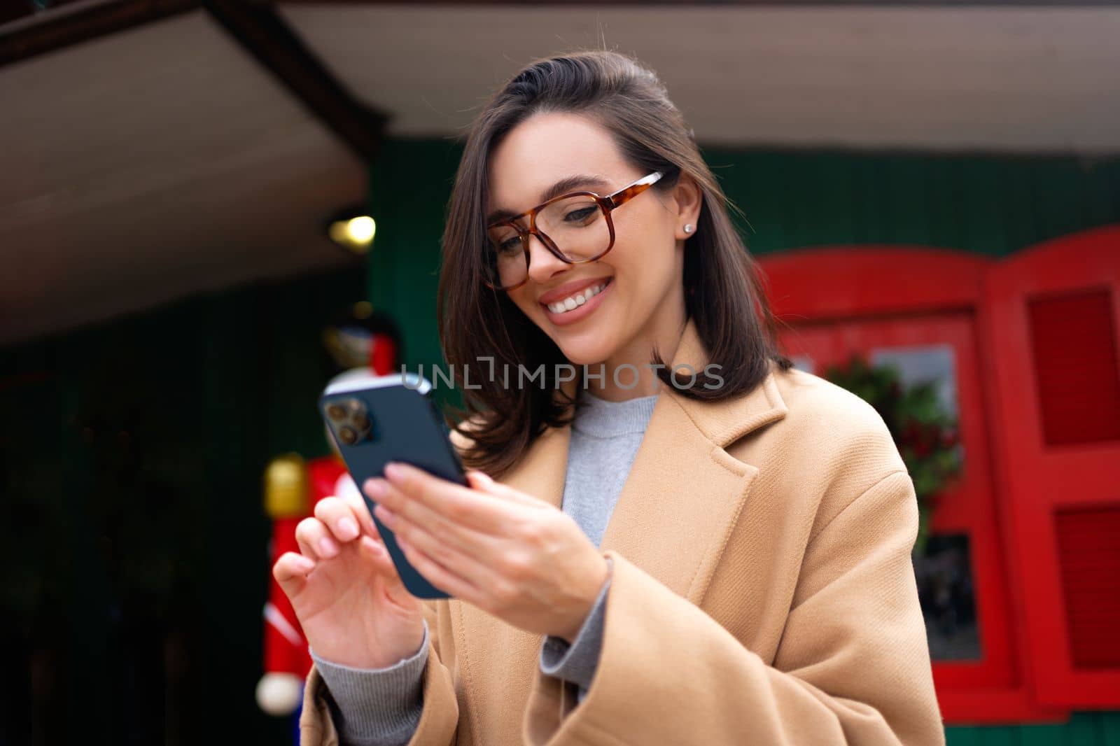 Woman using smartphone on christmas market. Caucasian female enjoying winter holiday season. Concept of social networking, communicating, using app. Looking device screen and smile. Holiday