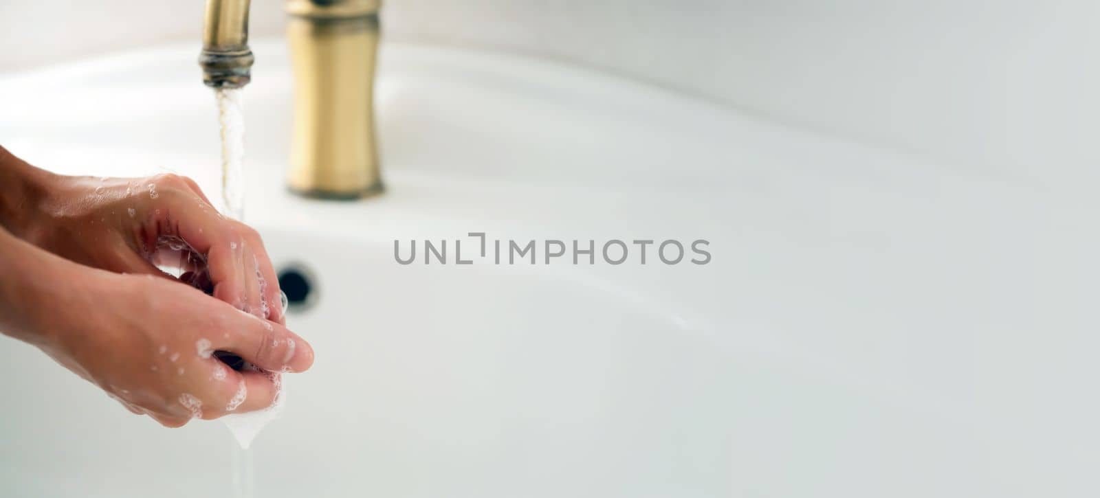 A young girl washes her hands thoroughly with soap under water in the bathroom, close-up view.