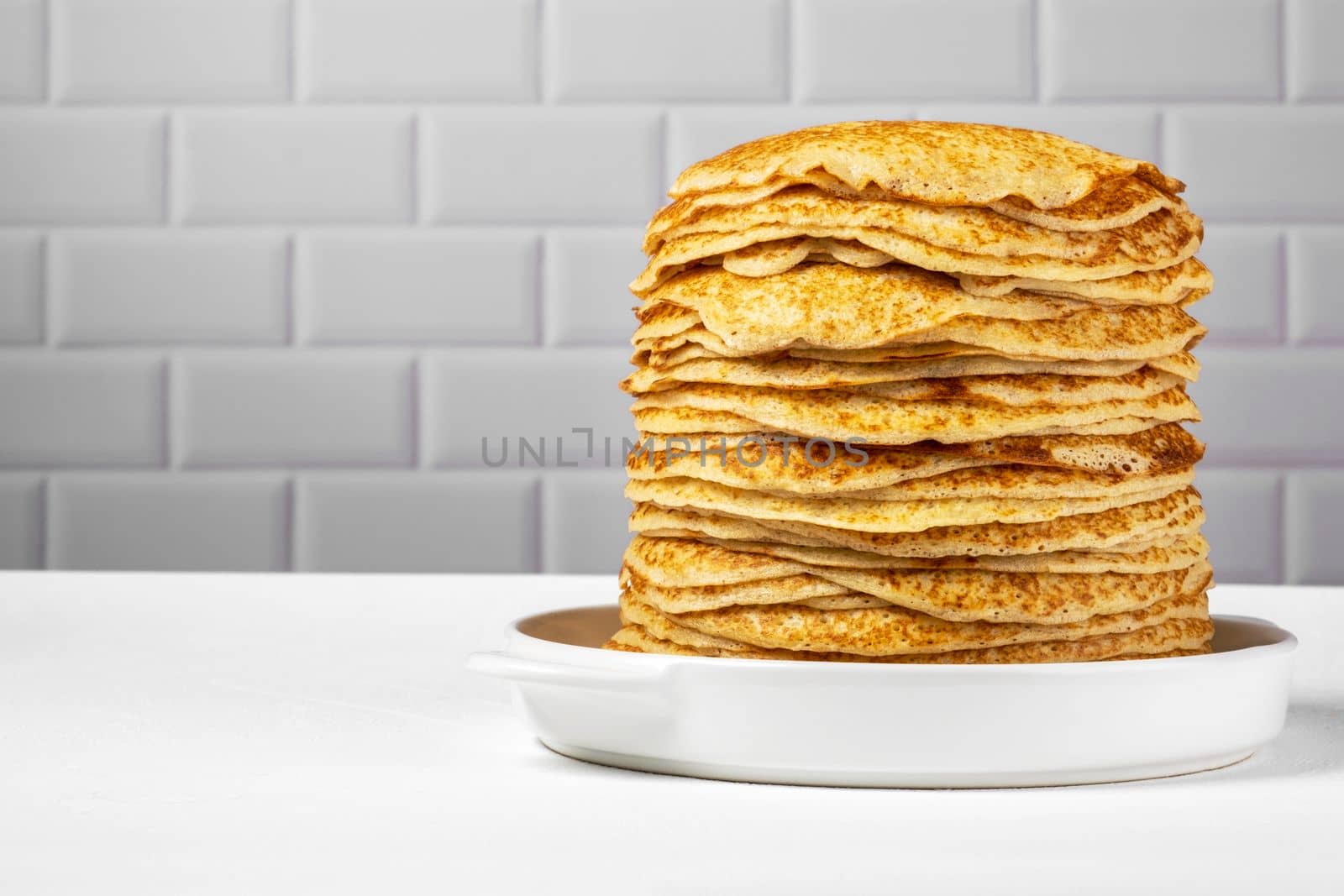 Stack of freshly baked pancakes lie in white ceramic form. Pancake week. Russian kitchen. Selective focus.