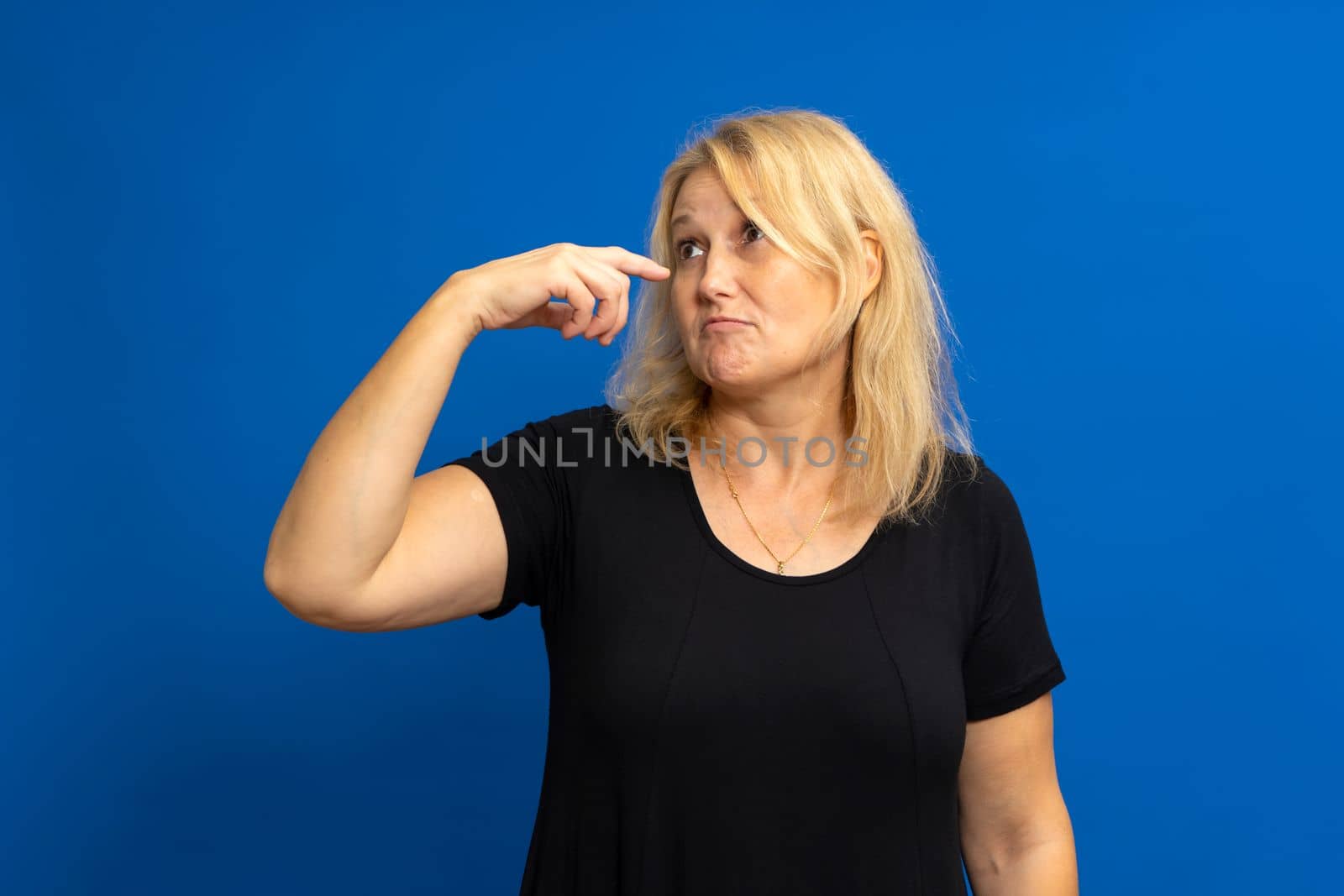 Photo of crazy amazed woman pointing index finger at herself, impressed, chooses news, isolated over blue tinted background