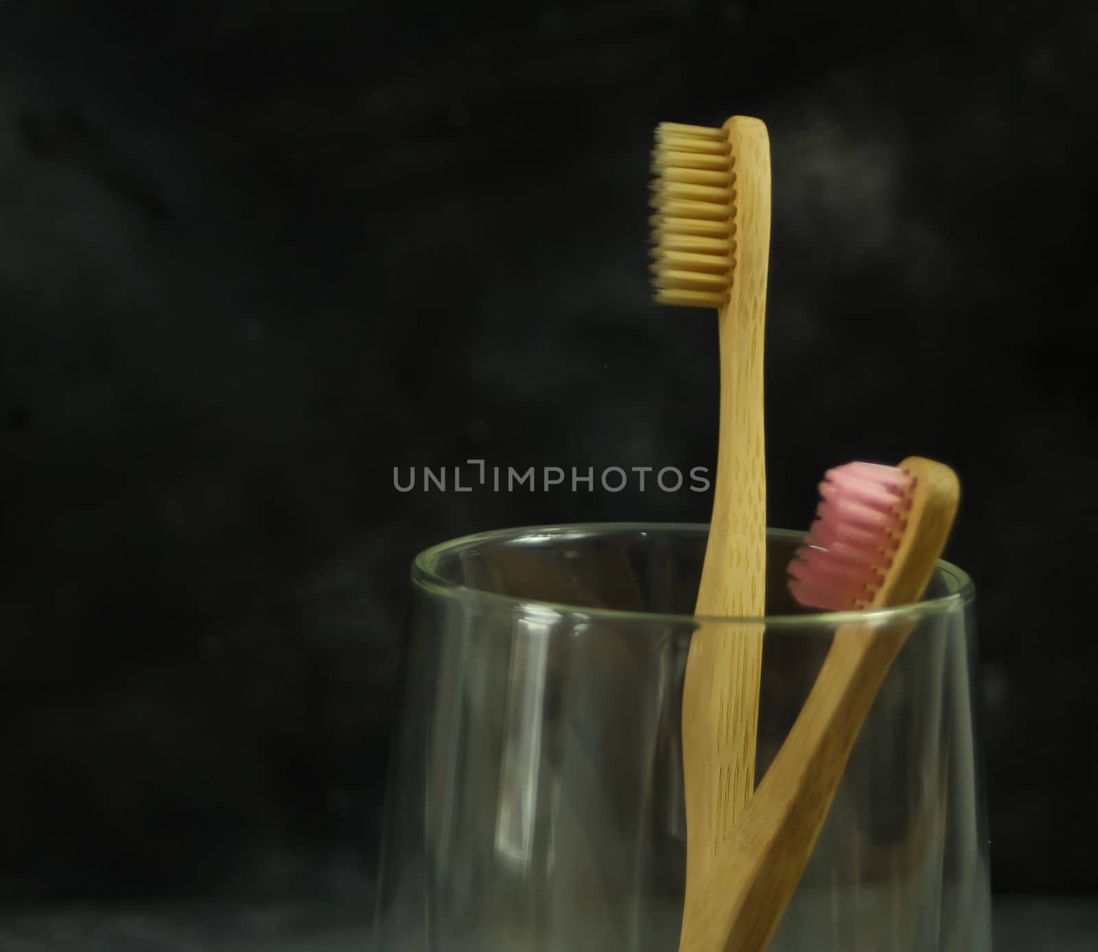Closeup view of eco-friendly bamboo toothbrushes on a glass on dark background
