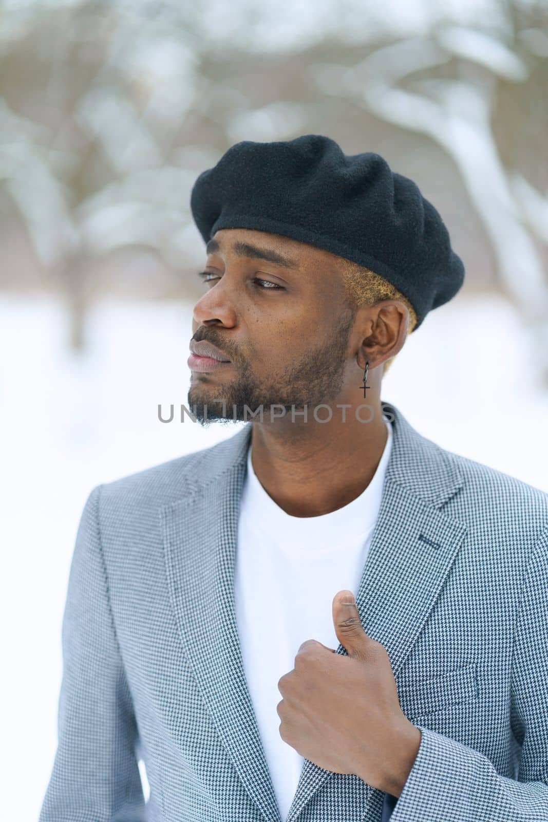 Young man in beret like Che Guevara stay on winter background. African american hold jacket looking aside. High quality photo