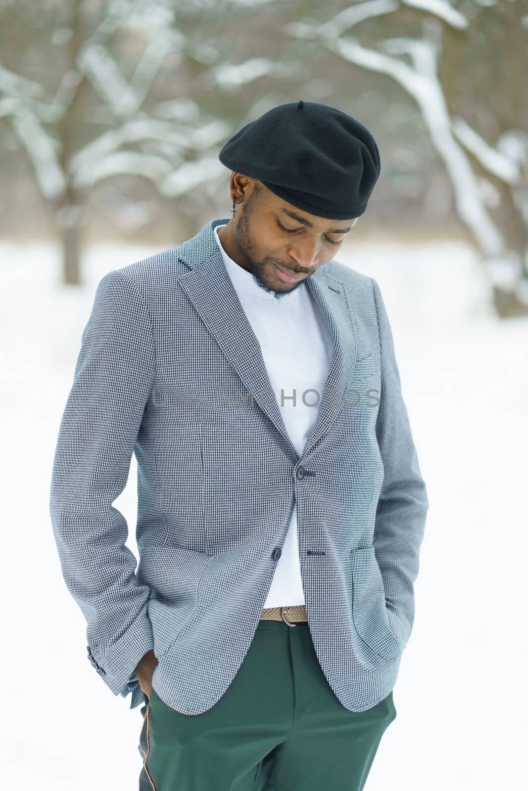 Sad african man stay in winter in snowy park. Young man in beret posing for camera outdoor. by LipikStockMedia