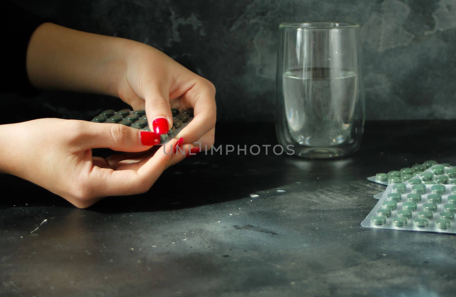 Woman hand taking spirulina tablet. Glass of water nearby. Concrete dark background