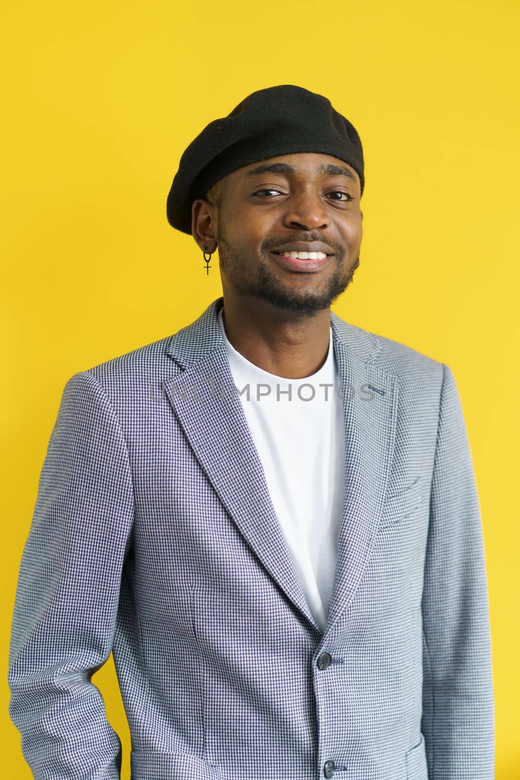 Happy handsome smiling to camera on yellow background. Young man in grey suit wearing black beret. Youth concept. by LipikStockMedia