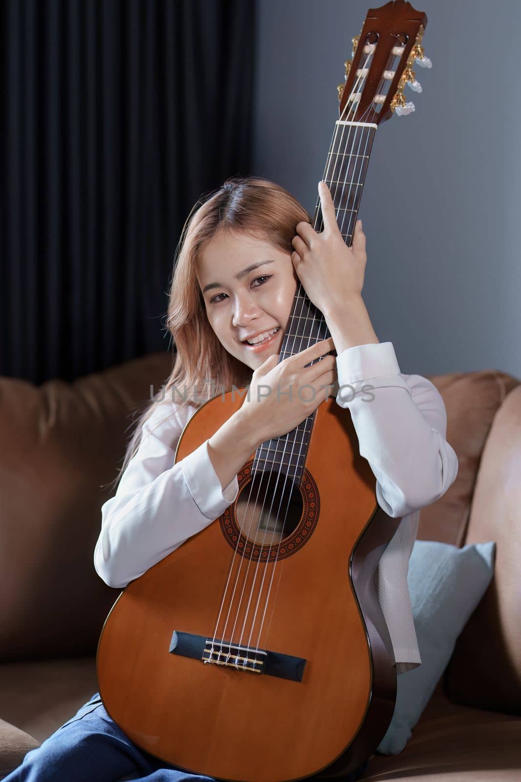 Portrait of young asian woman playing guitar on sofa relaxing stress on vacation.