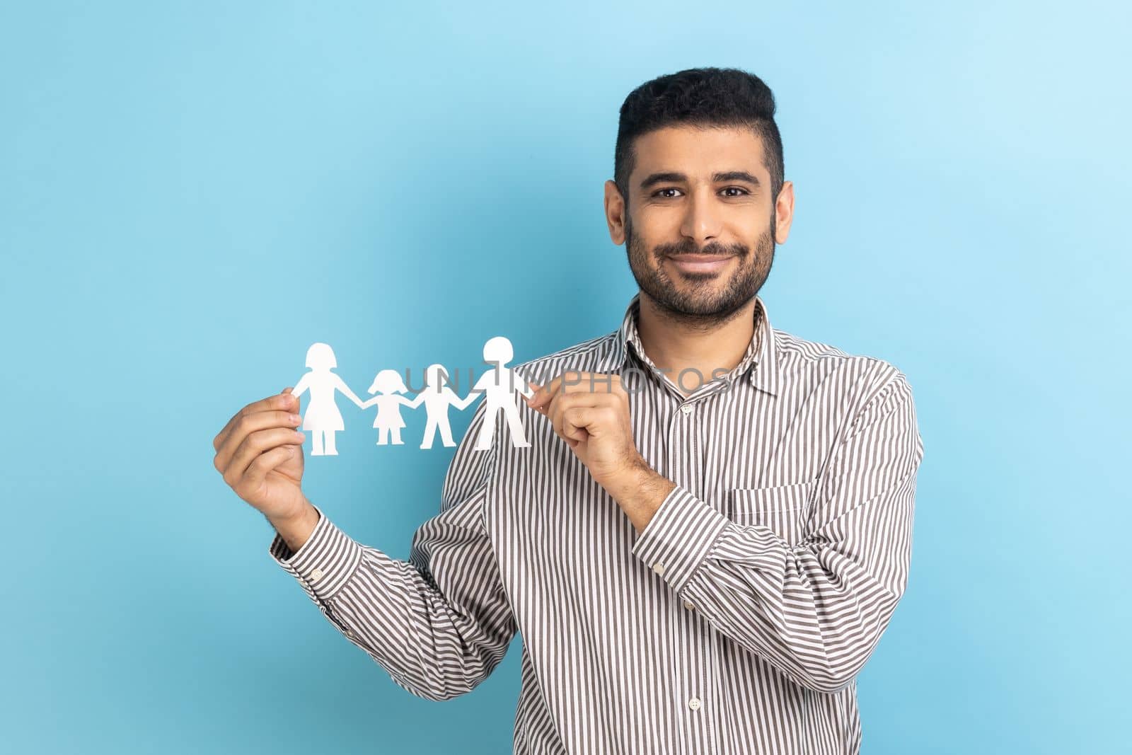Portrait of handsome bearded businessman holding paper chain in hands, concept of happy family, parenthood, childhood, wearing striped shirt. Indoor studio shot isolated on blue background.
