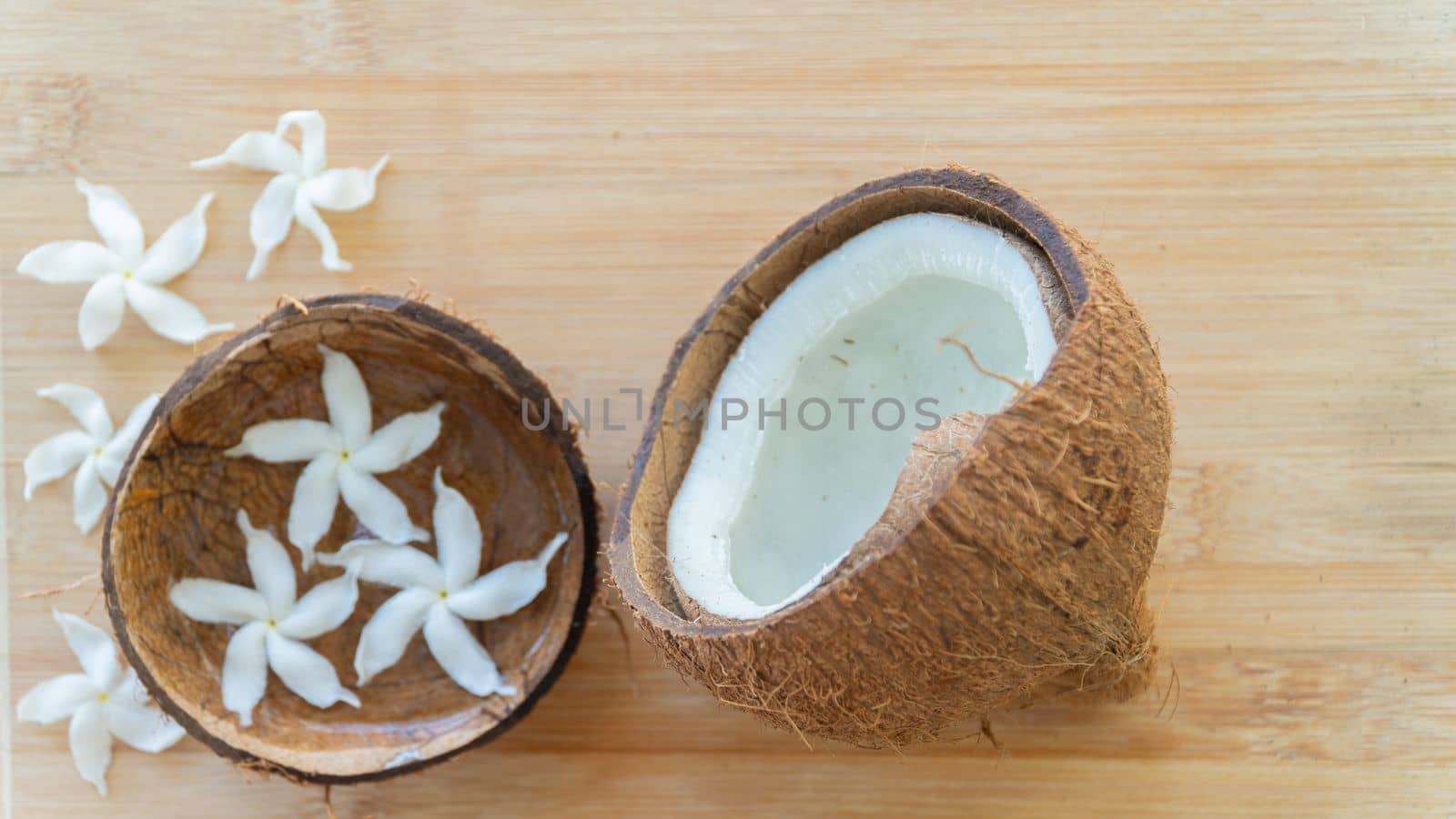 Open coconut nut on a wooden background with white flowers by voktybre