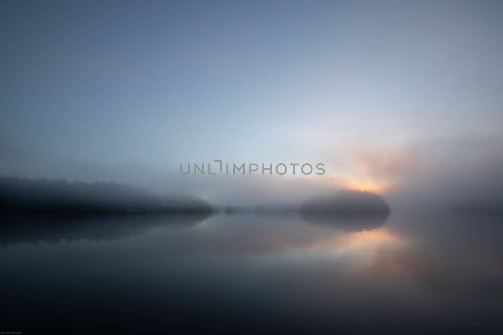 Morning fog with sun peeking through clouds and reflection in the harbour, Blunden Harbour, British Columbia, Canada. Fog on a harbour