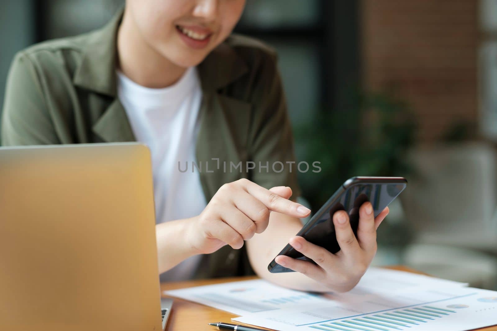 Young asian businesswoman uses a mobile phone to contact a customer, working hard at the office using laptop data graphs, planning for improvement, analyzing and strategizing for business growth. Business concept