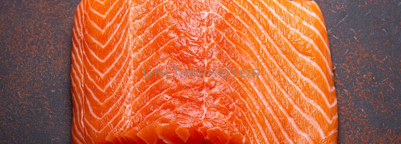 Piece of fresh Norwegian raw salmon fillet on dark brown rustic background top view, healthy nutrition and diet by its_al_dente