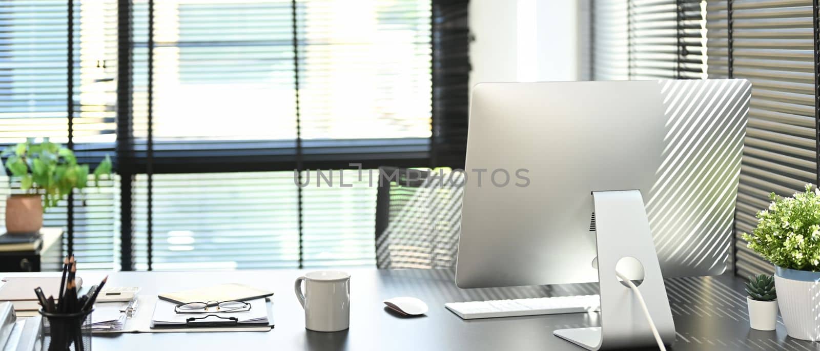 Modern office interior with computer, cup of coffee, document, supplied and potted plant on blank wooden table.