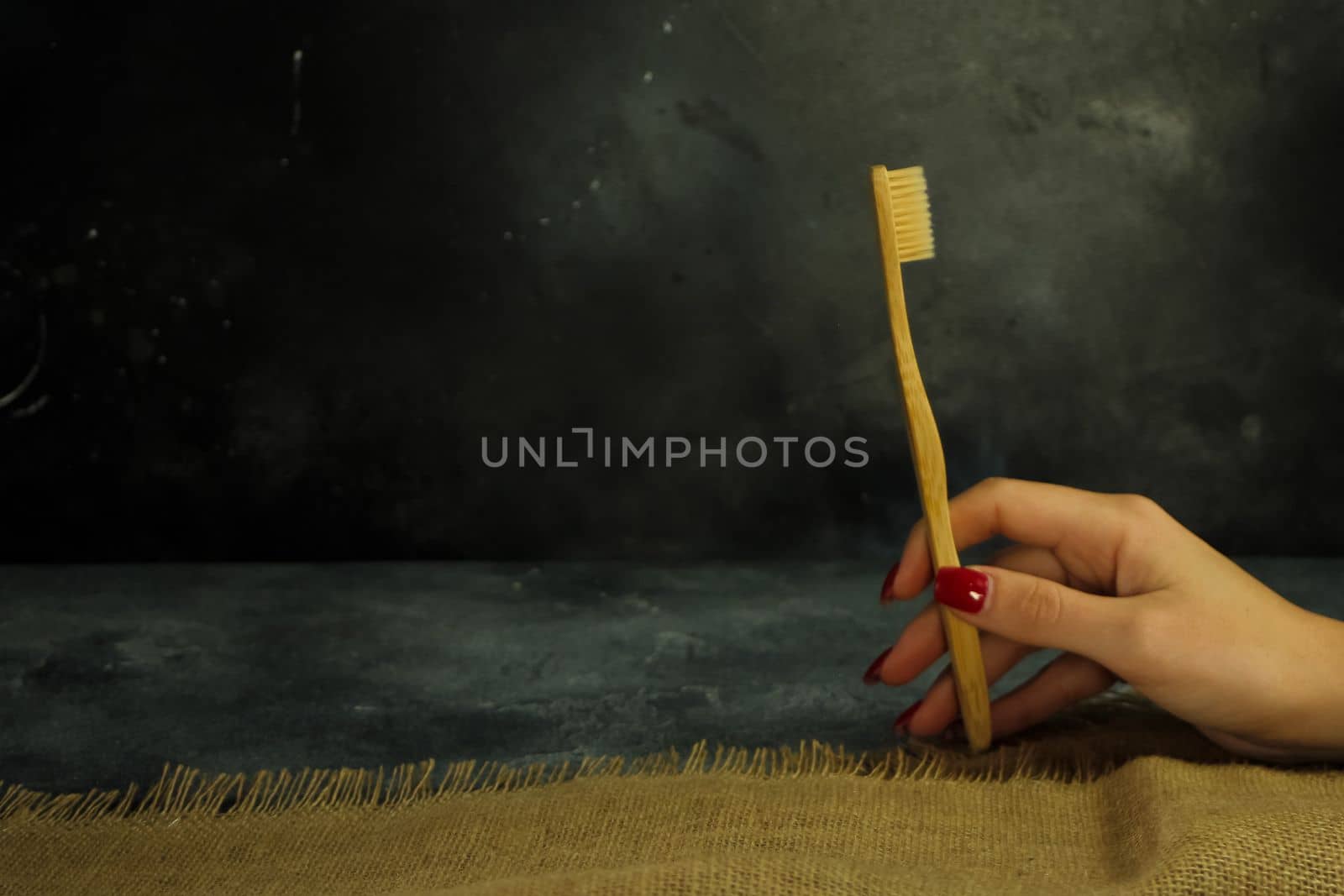 Woman hand holding eco-friendly bamboo toothbrush on a dark background