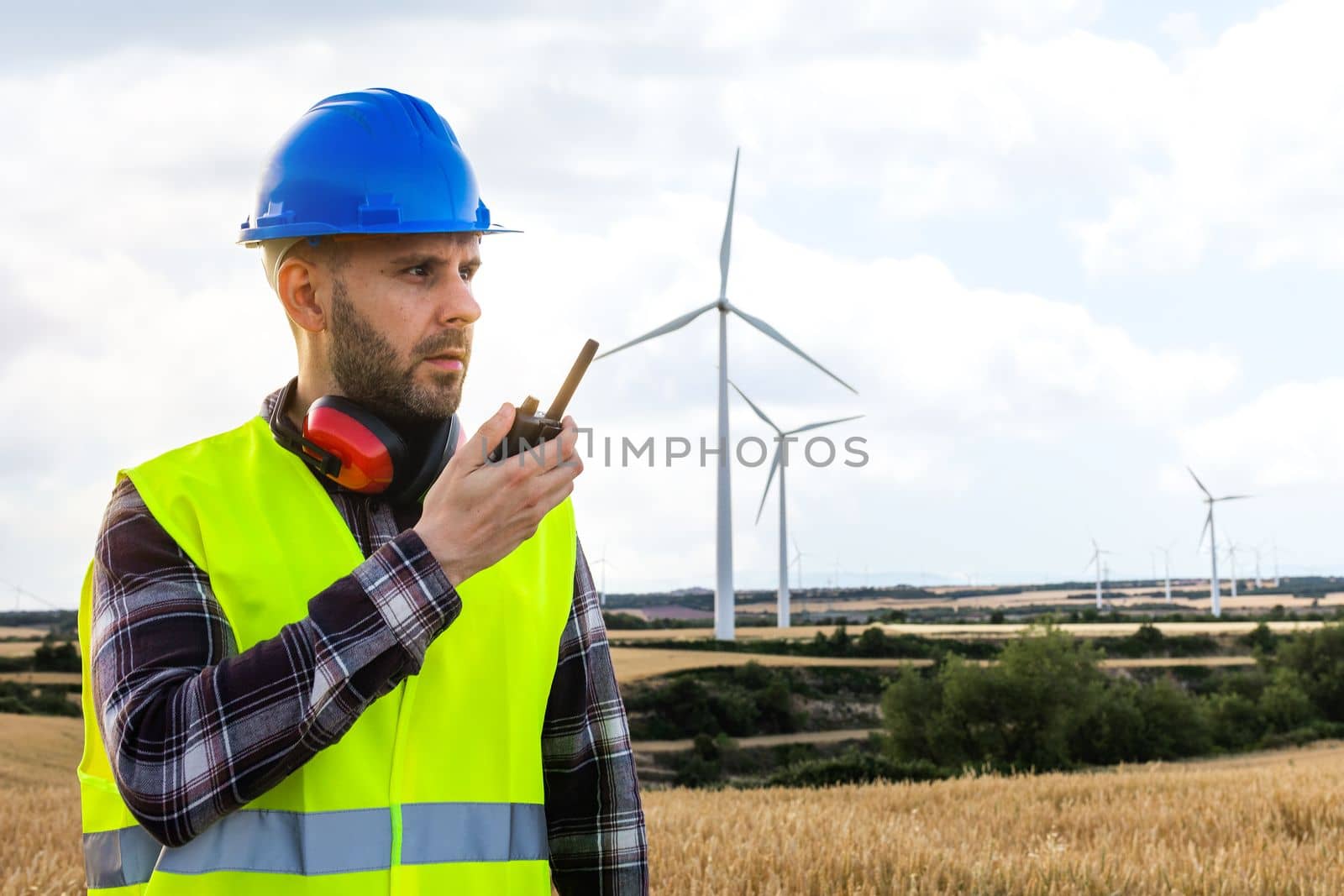 Male maintenance worker in wind turbine farm communicating with walkie-talkie. Copy space. Renewable energy concept.