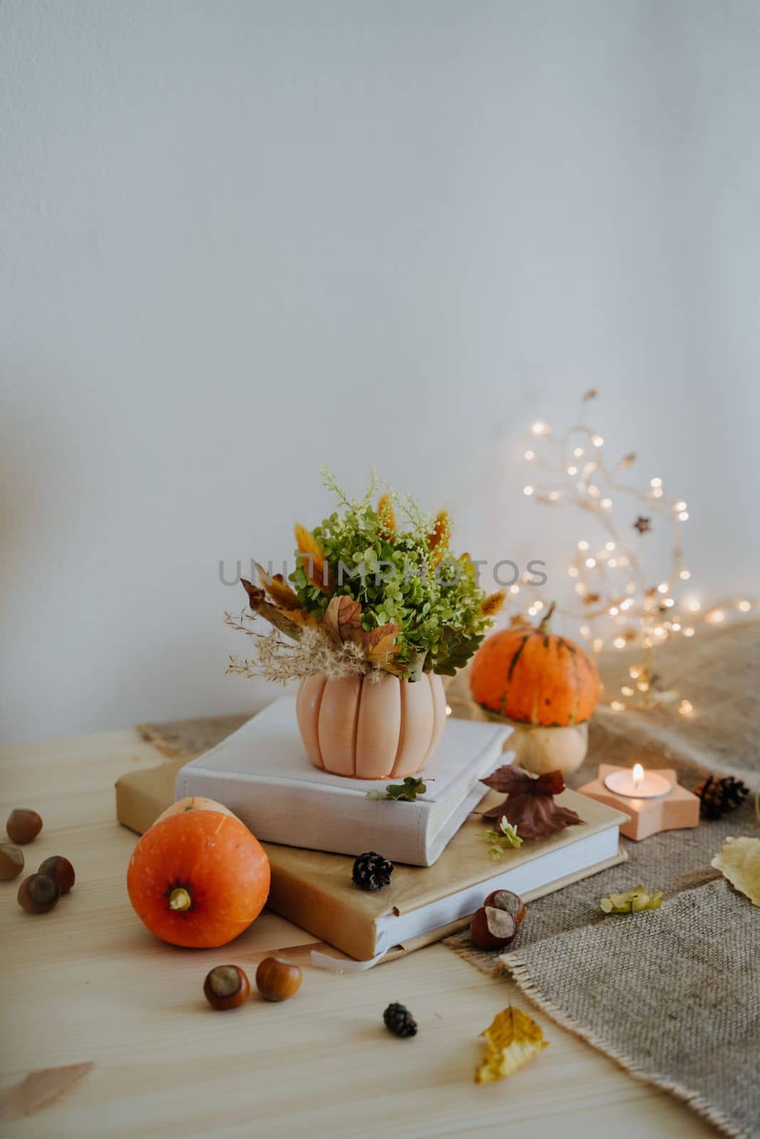 Autumn composition of books, pumpkins, nuts, autumn leaves, a bouquet of dried flowers, cones. Pumpkin and nuts. Garland with warm light. Yellow Bokeh. Thanksgiving Day. Vertical photo.