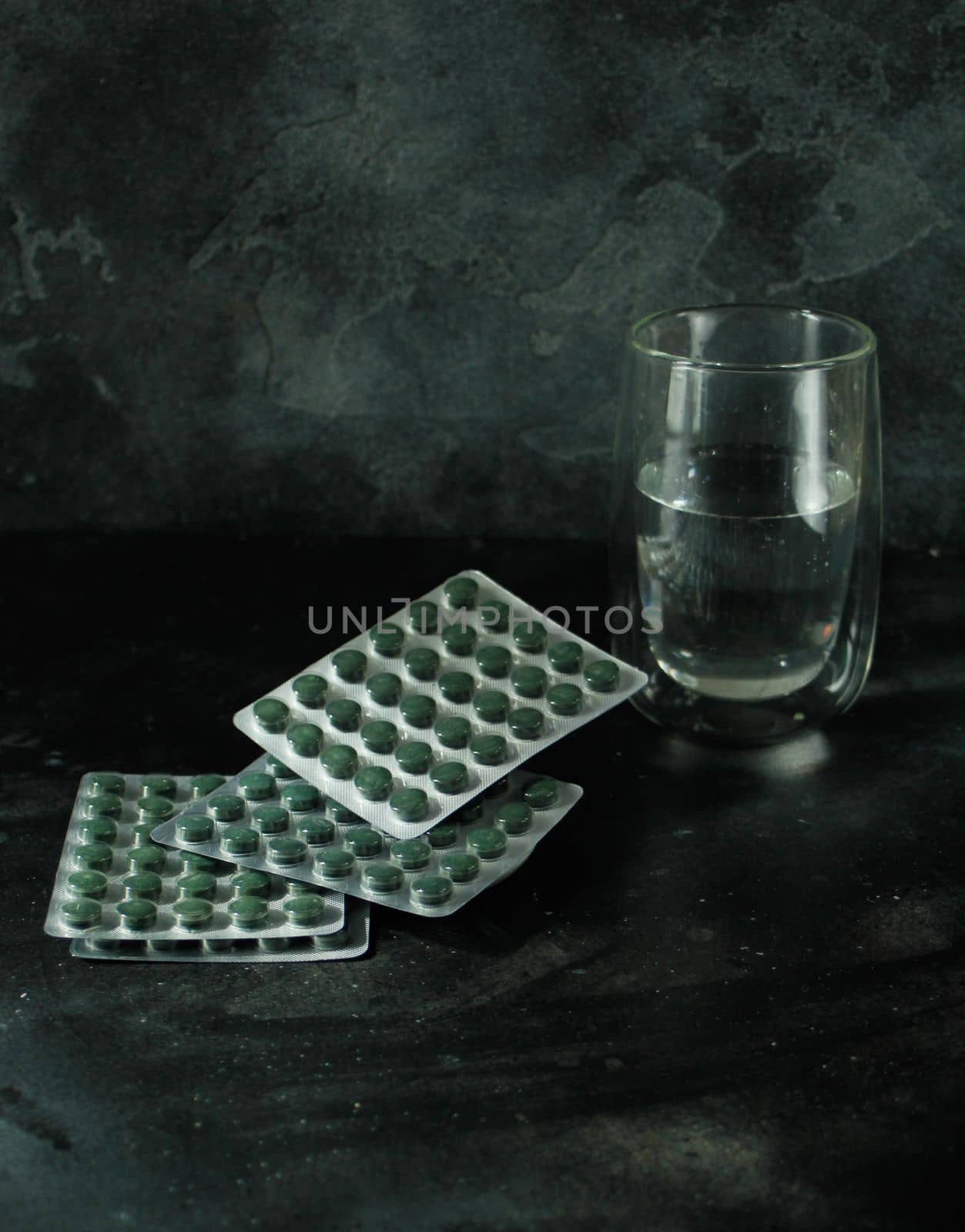 Chlorella or spirulina tablets and a glass of water on dark background by danjelaruci