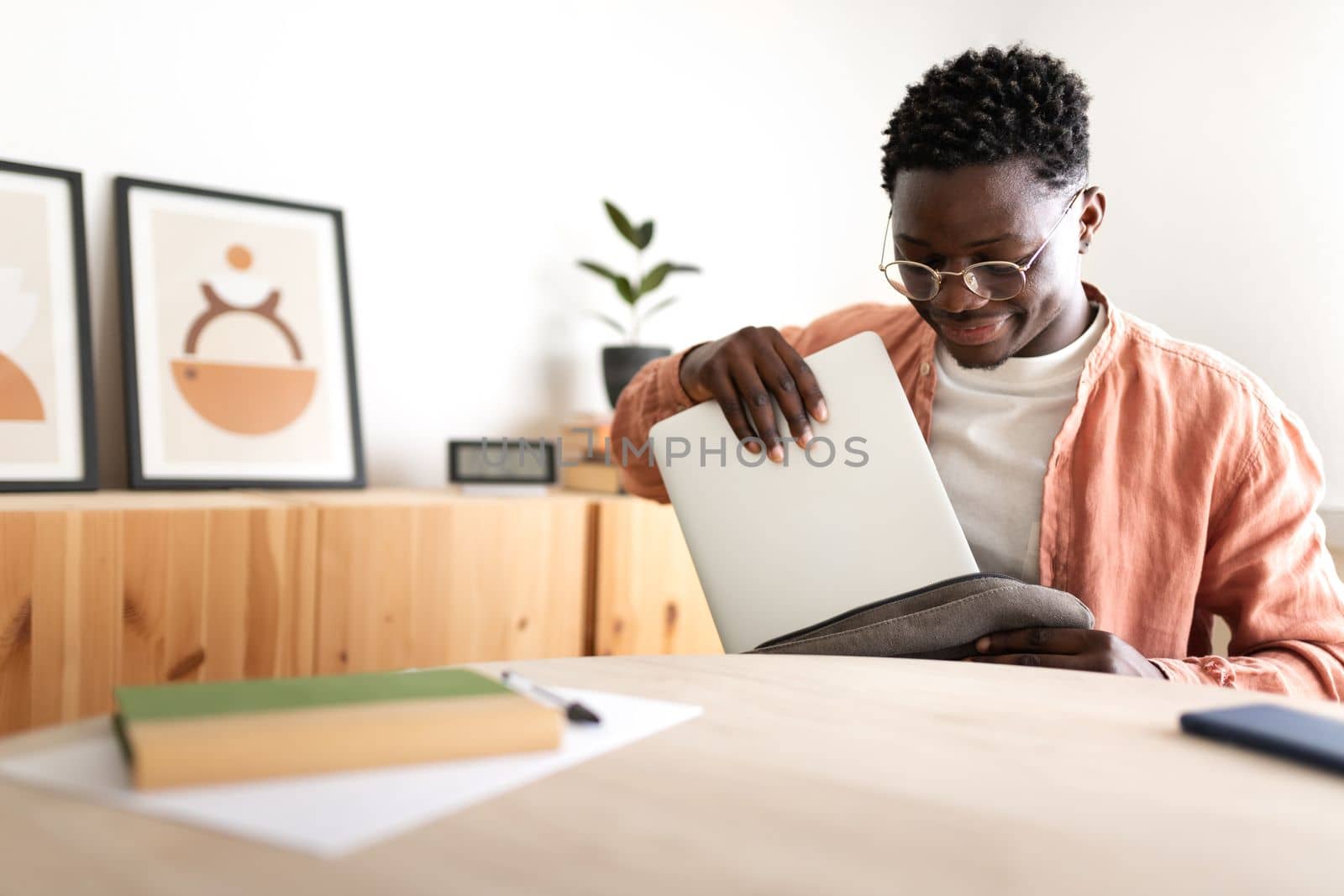 Black male high school teen student removing laptop out of backpack to start studying at home. Copy space. Education concept.