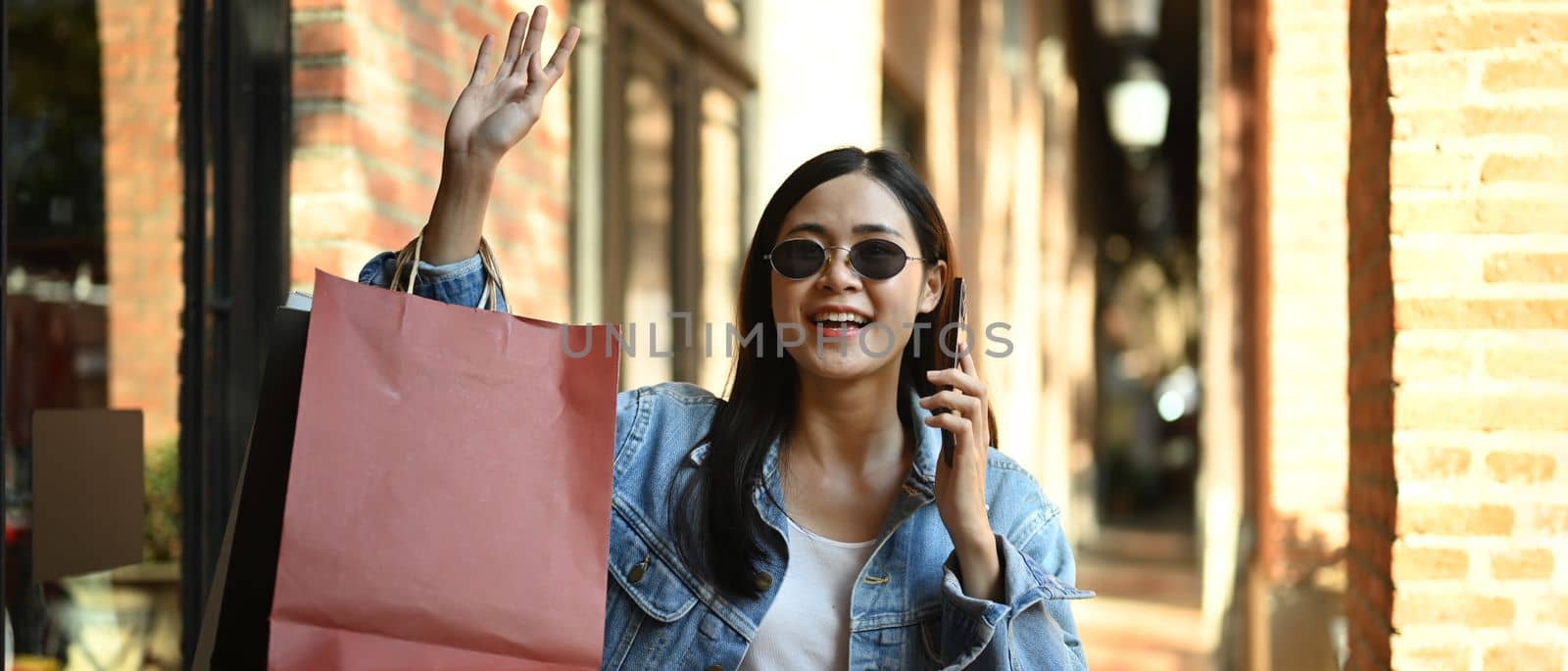 Shot of fashionable woman carrying shopping bags and talking smart phone at outdoor on sunny day.