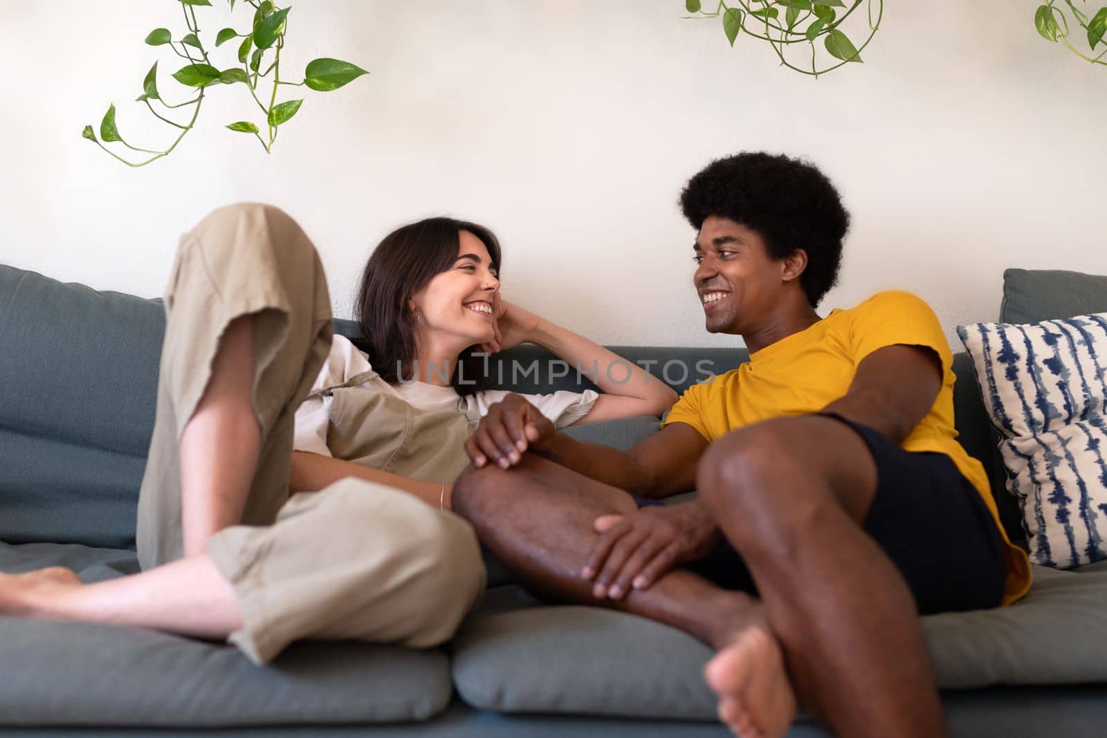 Happy young multiracial couple in love looking at each other relax lying on the sofa. Lifestyle concept.
