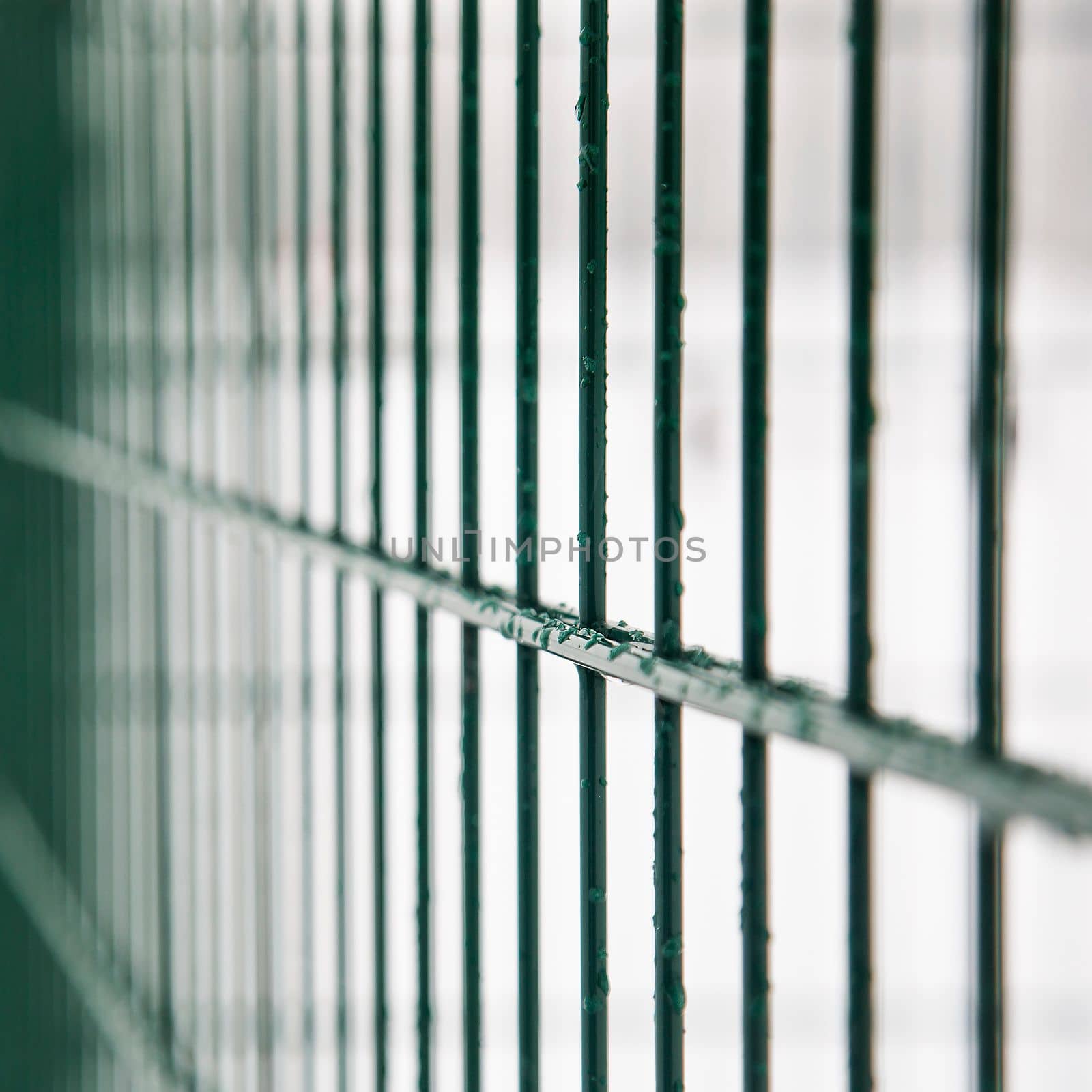 Metal fence with frozen water in winter. An icy barrier on a light background. Green fencing. Close-up.