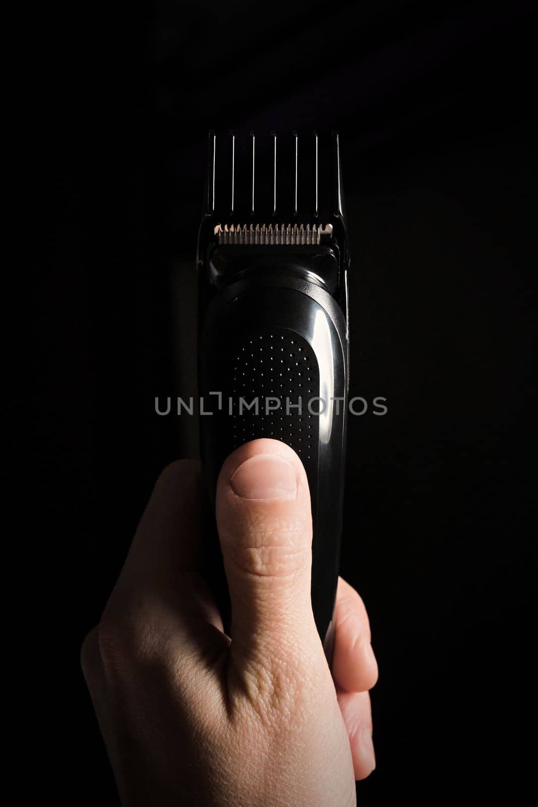 Close-up of Electric shaver machine with nozzle in hand on black background, copy space, vertical.