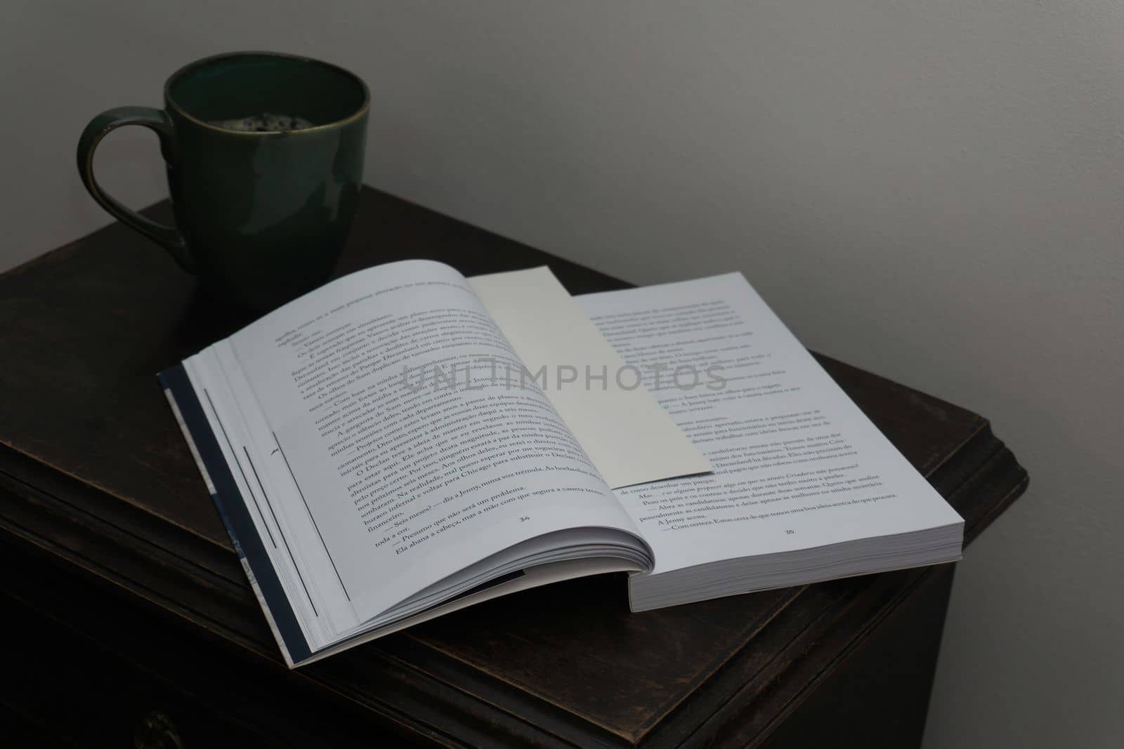 Open book and coffee cup on antique bedside table