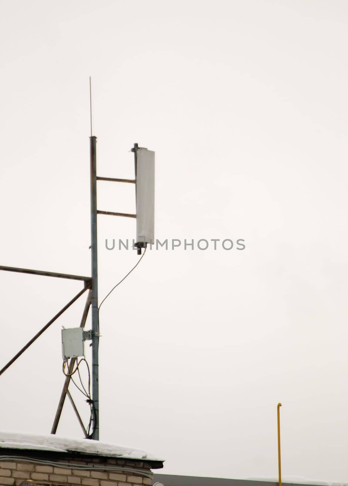 A cellular antenna on the roof of the house provides a reliable connection. Snow lies on the milestone, against the background of a gray sky. Cloudy, cold winter day, soft light.