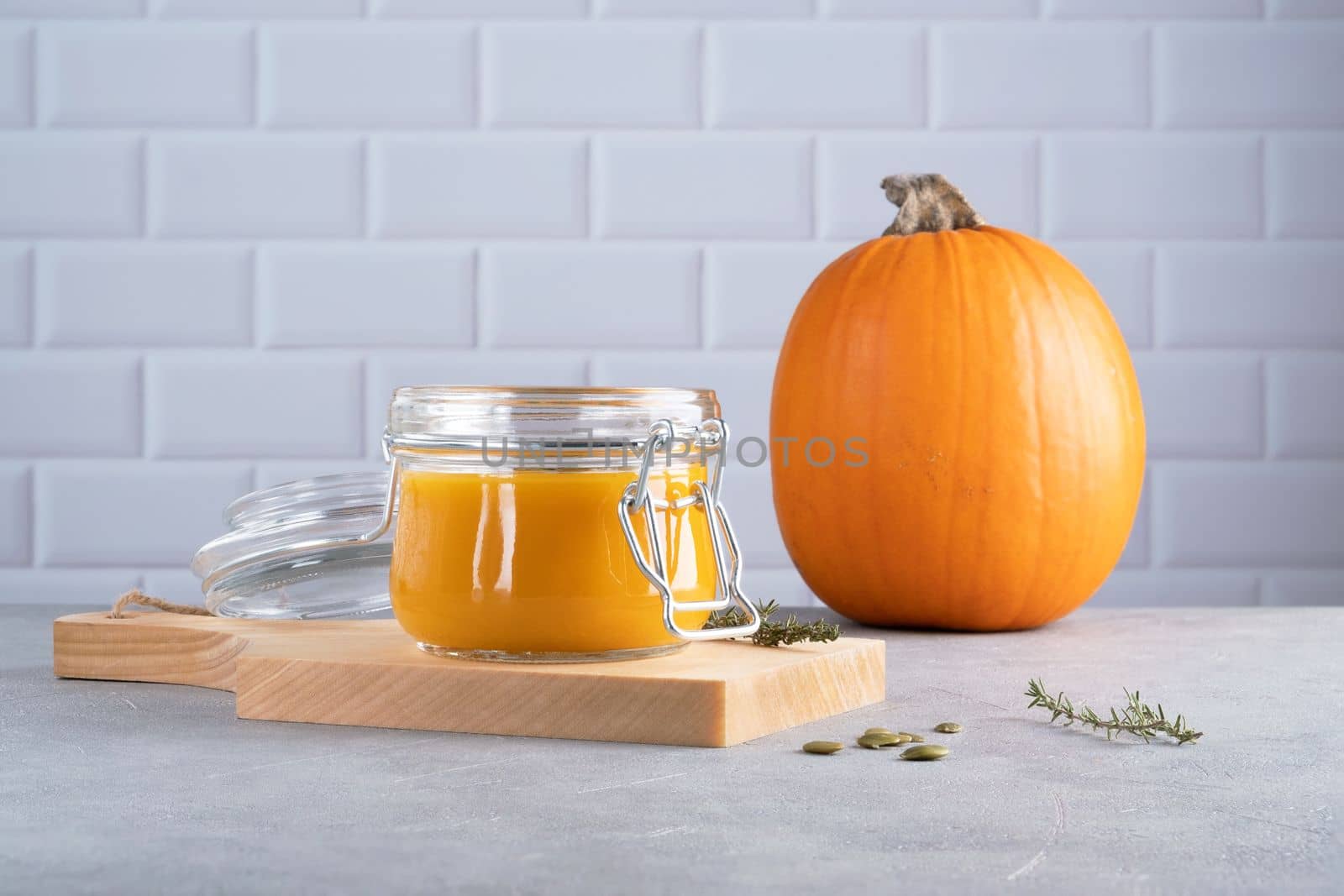 Pumpkin puree soup with pumpkin seeds and thyme in a glass jar on a wooden kitchen board. Ripe pumpkin. Healthy diet. Selective focus.