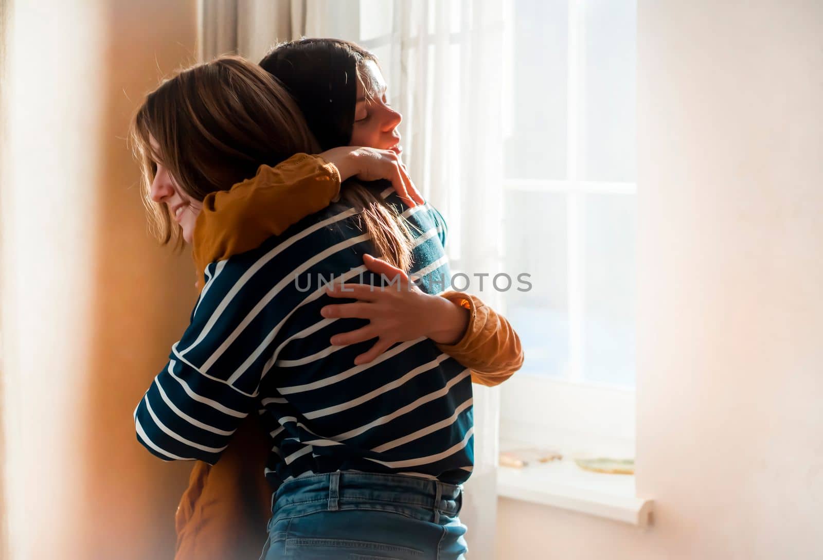 Two female friends of different ethnicity are embracing in the sun and happy to meet each other. Girls celebrate the holidays and hug tightly and warm, feel an emotional connection and love.