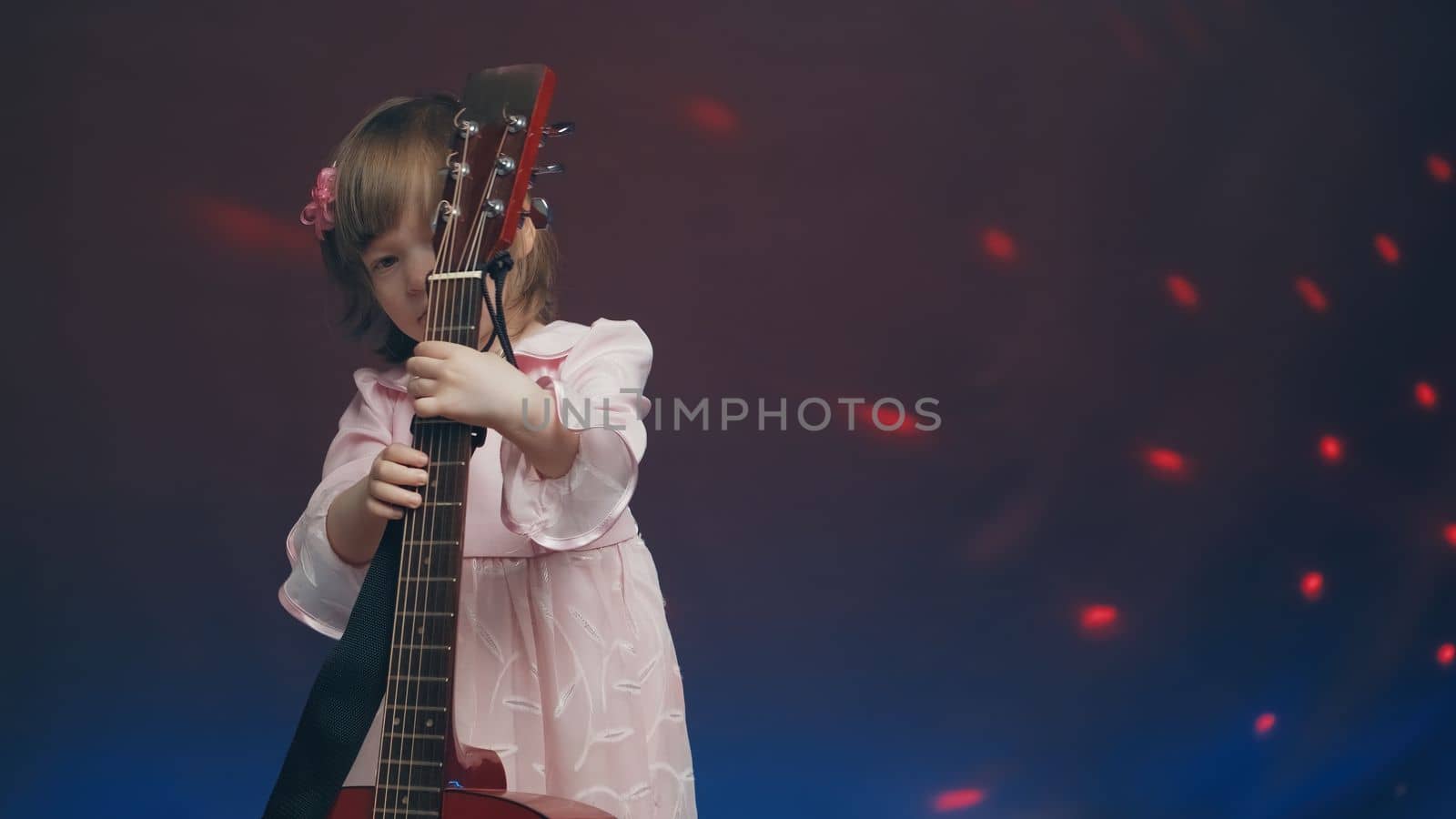 Cute little girl stands on stage in vintage dress and plays an acoustic guitar like a counter bass or cello. The concept of performing the author jazz and blues music. Hobbies and art among children