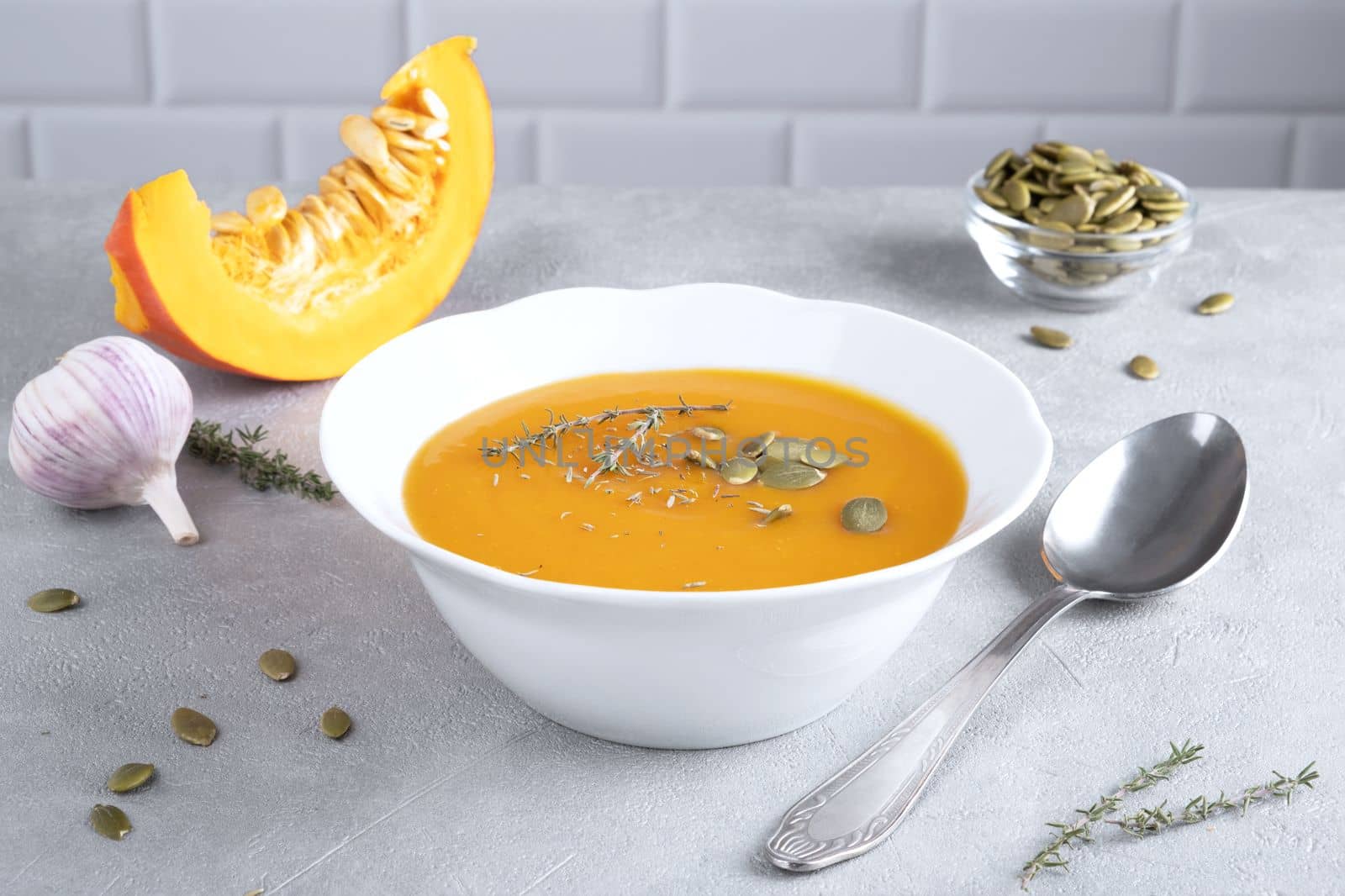 Pumpkin puree soup with pumpkin seeds and thyme in a white plate and a piece of ripe pumpkin. Healthy diet. Selective focus.