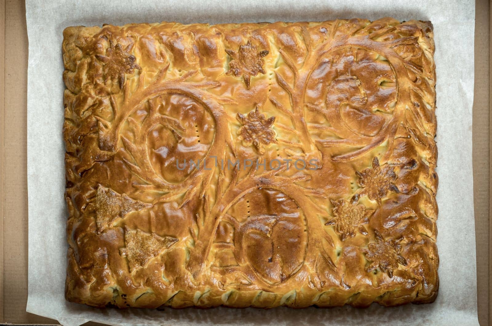 Top view close-up decorated yeast dough pie with stuffing in a cardboard box. Food delivery, fresh baked goods. Selective focus.