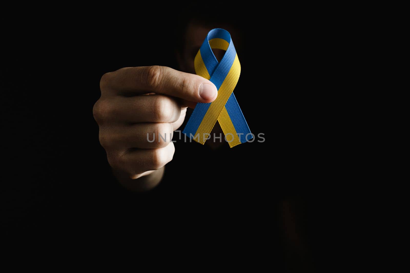 male hand holds yellow and blue ribbon on dark background. concept needs help and support, truth will win