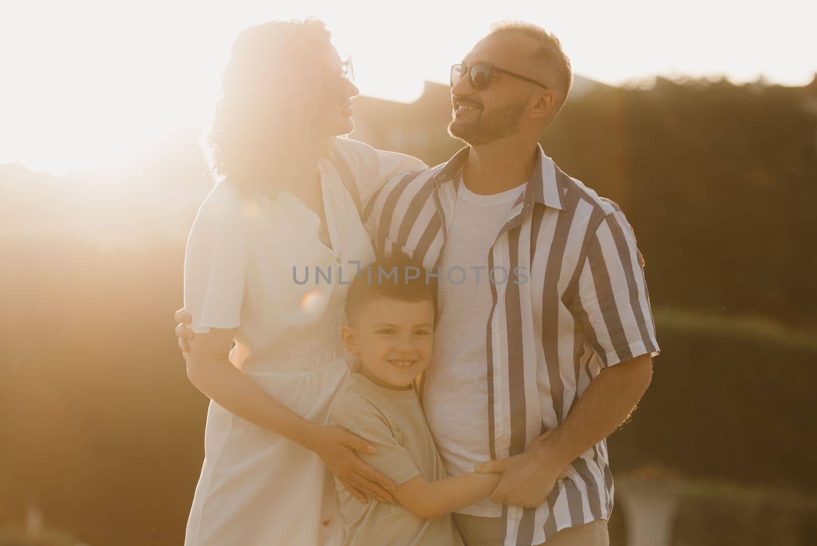 Father, mother and son are hugging in an old European town. Happy family in the evening. Dad is smiling at his family at sunset.